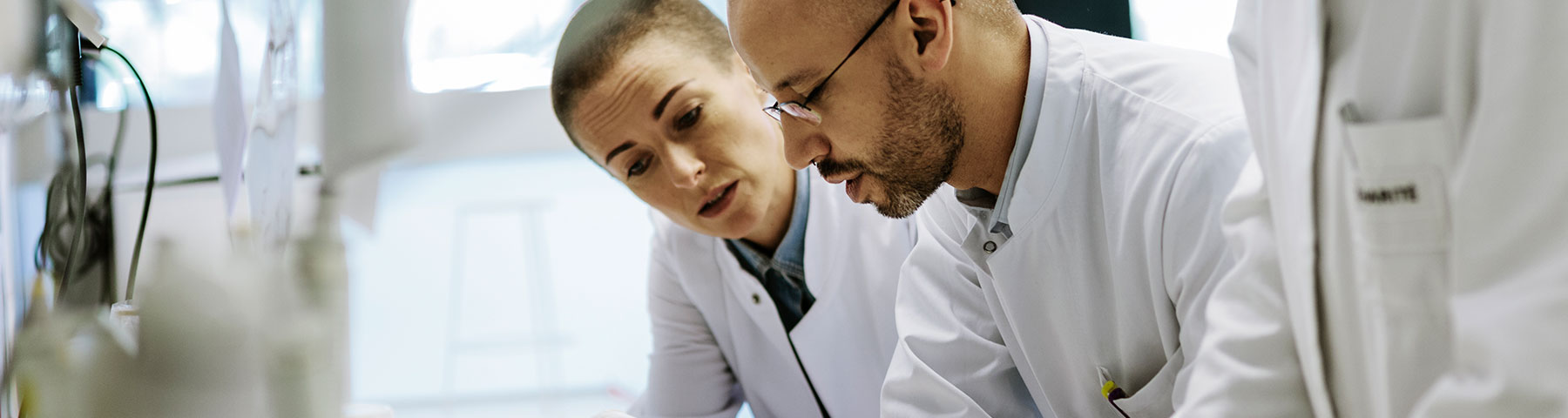 Two scientists in white lab coats collaborating in a laboratory setting, analyzing data or conducting research.