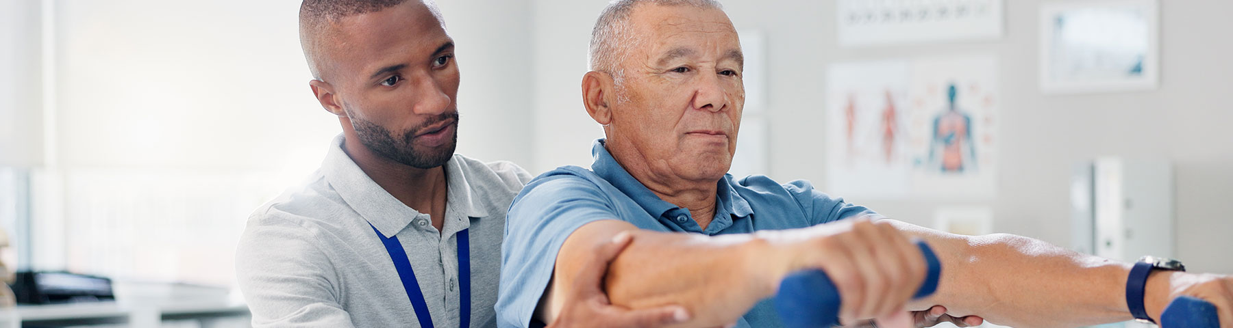 A physical therapist assisting an elderly man with arm exercises using small dumbbells in a rehabilitation setting.