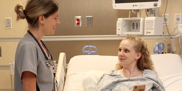 A nurse talking to a smiling female patient at bedside.